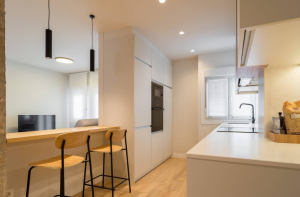 Cuines petites amb molt de gust. OB CUINES. Tens moltes idees, però pocs metres? Sortim al rescat! Estem convençuts que, ben planificada, una cuina petita pot ser tan funcional, acollidora i bonica com una de grans dimensions. Et convidem a deixar de veure la mida com un límit, sinó com una oportunitat per esprémer la creativitat i aprofitar cada racó sense renunciar a l'estil que vols. Per demostrar-t'ho, avui t'ensenyem tres exemples dels que millor saben de planificació de cuines: els nostres distribuïdors. Continua llegint per descobrir que una cuina petita pot donar molt, però que molt de joc. Oberta, compacta i connectada al saló La primera cuina és un exemple perfecte de com es pot integrar visualment i estèticament una cuina sense perdre gens ni mica de funcionalitat. Es tracta d'un projecte signat per l'estudi d'interiorisme donostiarra “APAL” i hi trobem un espai compacte, amb les zones de treball i emmagatzematge distribuïdes en paral·lel. El gran detall diferenciador en aquest cas és que aquesta cuina es comunica amb el saló mitjançant una va oberta en què han instal·lat una barra on es pot menjar mirant al saló. Aquest element no només amplia la sensació d'espai, sinó que actua com a punt de connexió entre les dues estances: perfecte per esmorzar, xerrar mentre es cuina o gaudir d'un cafè amb vista sobre el saló.